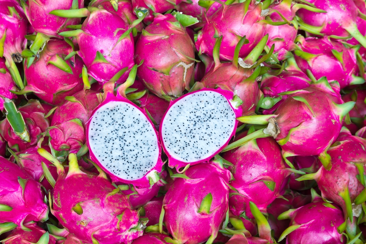 Pile of pink dragon fruits with one fruit cut in half on top of the pile
