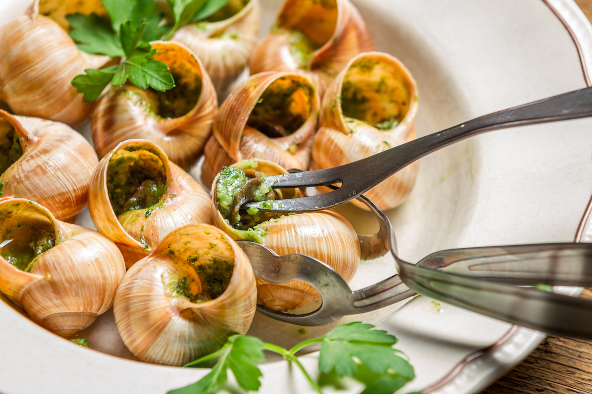 Bowl of escargot in shells with garlic butter and serving fork.