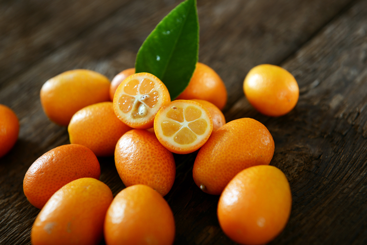 Pile of kumquats on a wooden background with one cut in half crosswise to reveal the juicy orange segments and small seeds