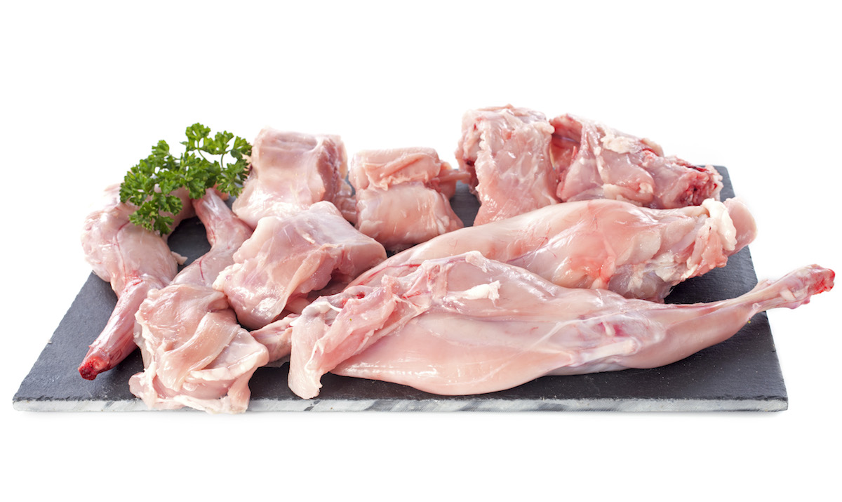 Raw rabbit meat on a black platter with white background
