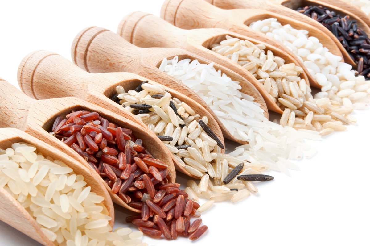 Wooden scoops with different types of rice on them on white background