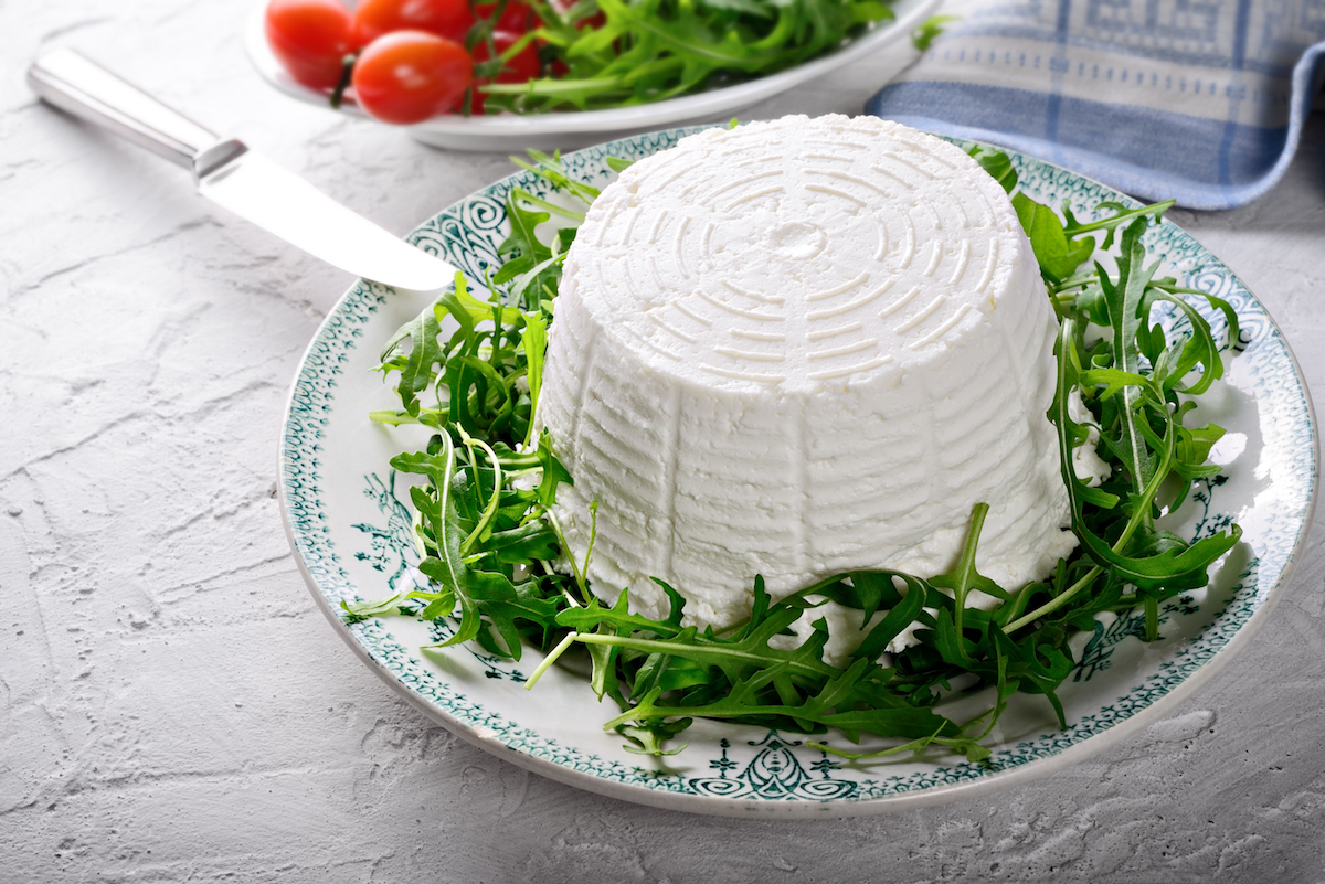 Homemade ricotta cheese on a white platter over a bed of arugula