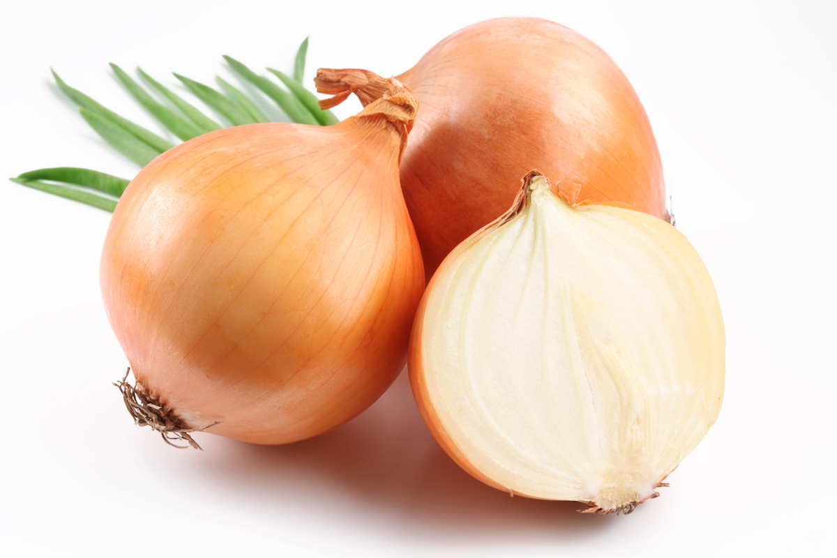 Two whole yellow onions on a white background with one yellow onion sliced in half vertically
