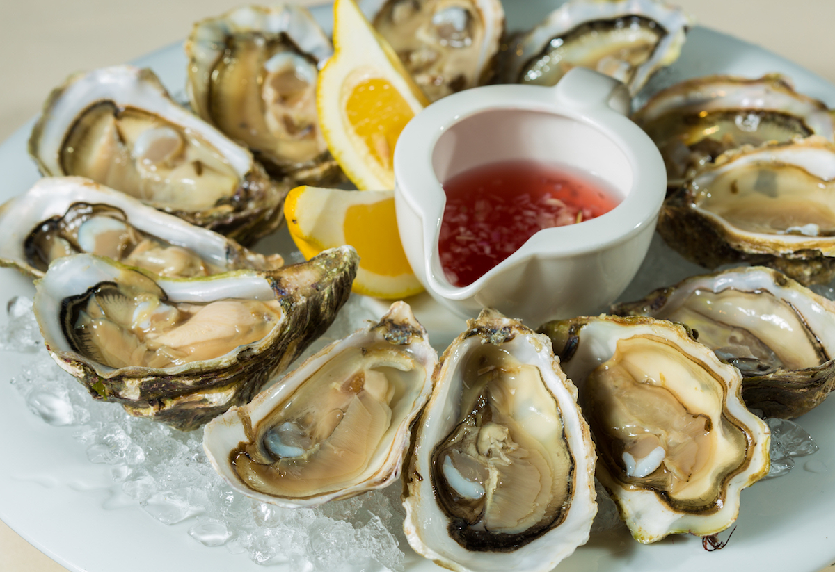 Platter of raw oyster halves on ice with lemon and mignonette sauce.
