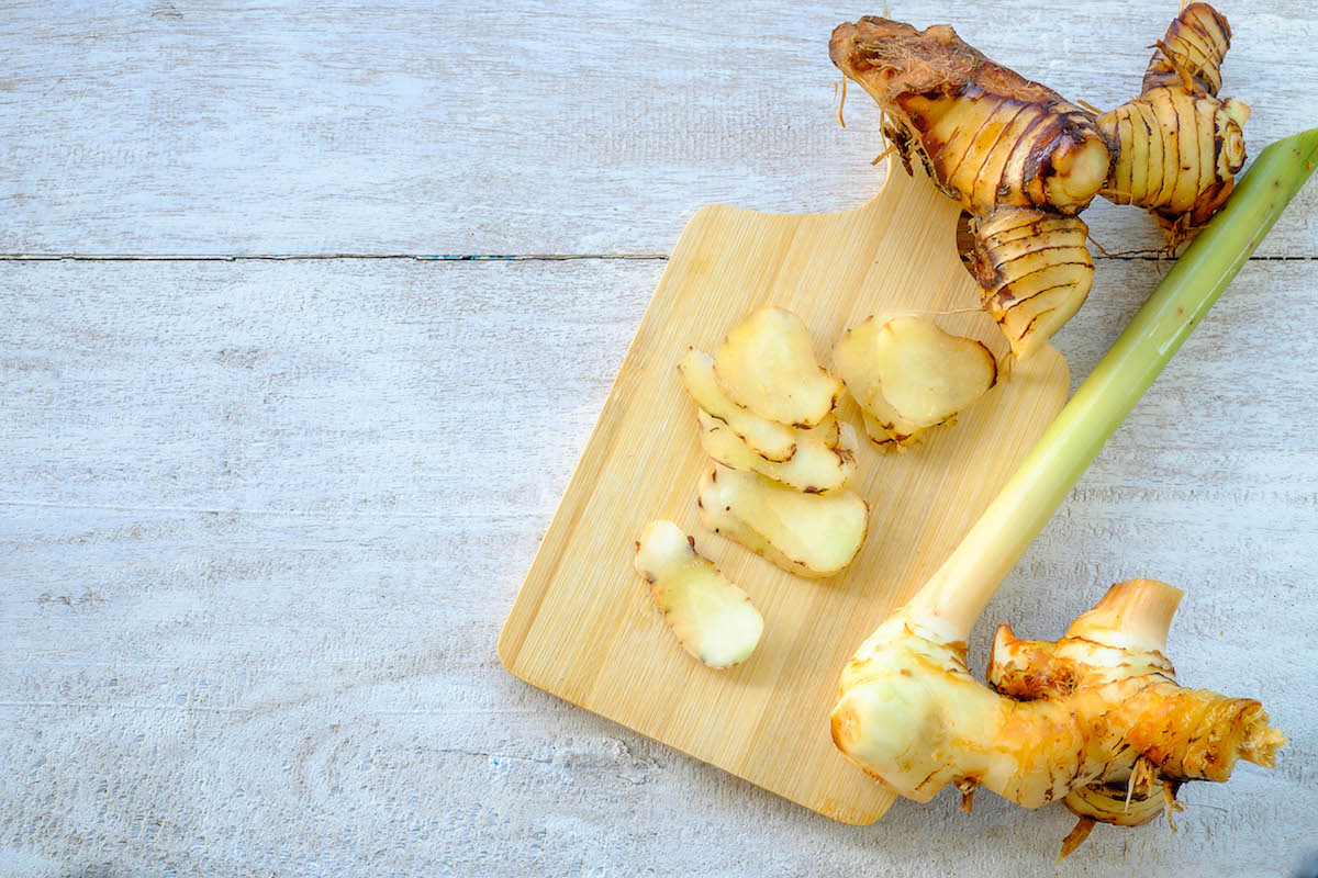 Fresh galangal root and stalk on a wooden cutting board.