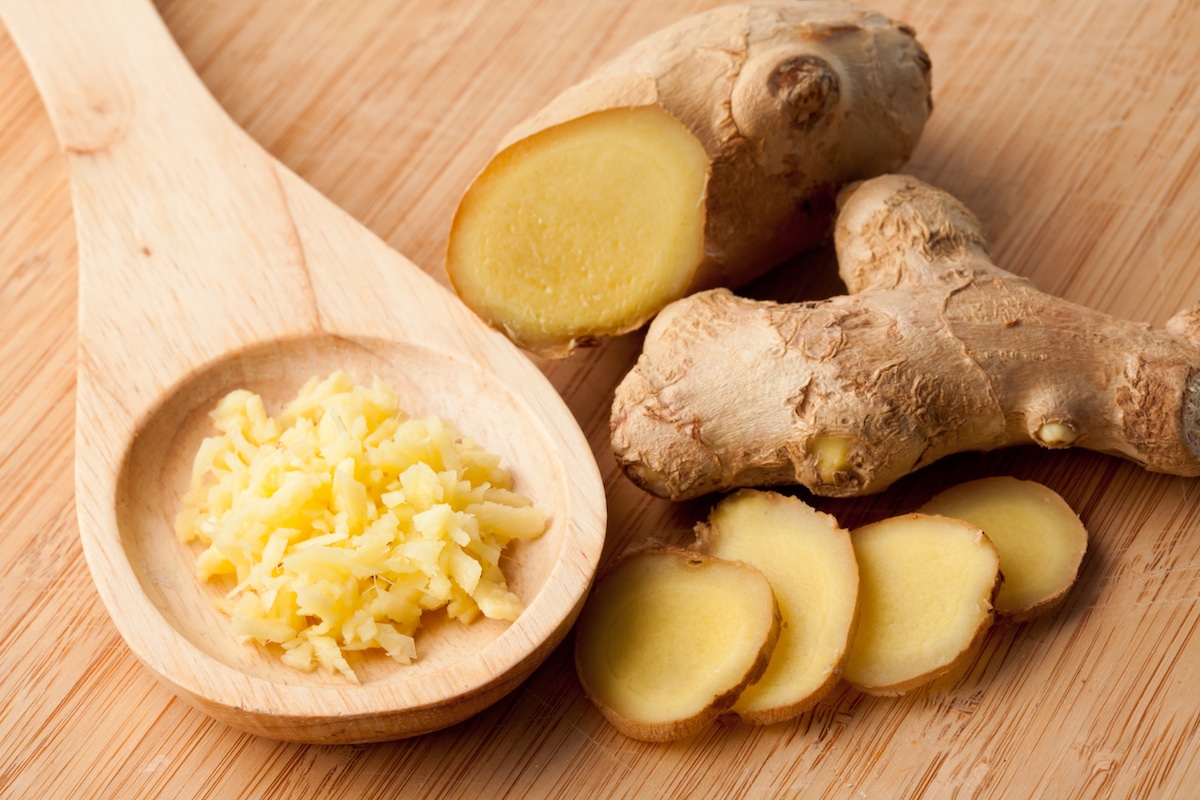 Fresh whole ginger root, sliced ginger, and minced ginger on a large wooden spoon