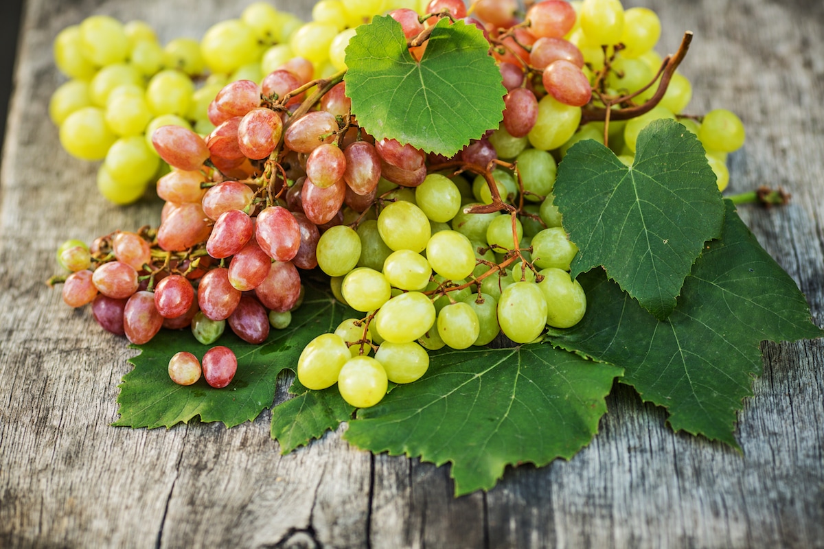 Ripe green and red grapes on a wooden table outdoors.