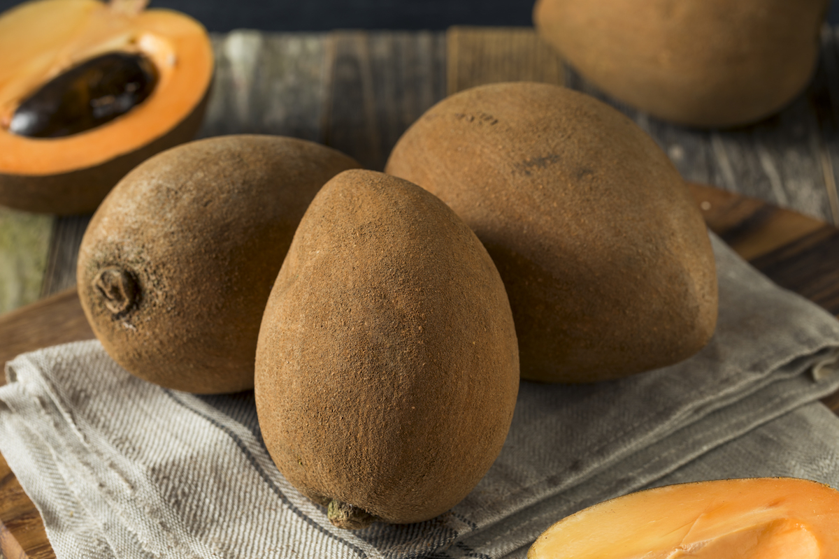Three brown mamey fruit on a wooden table