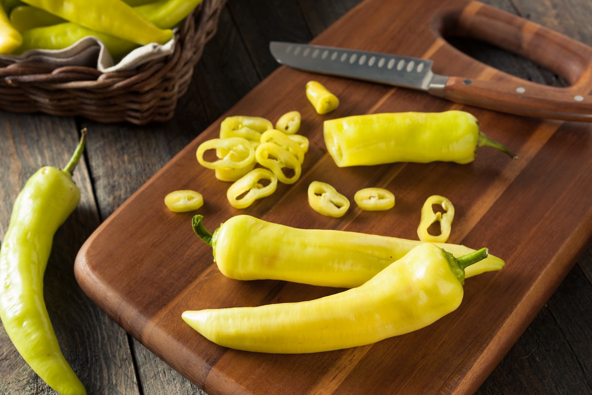 Fresh whole banana peppers on a wooden cutting board.