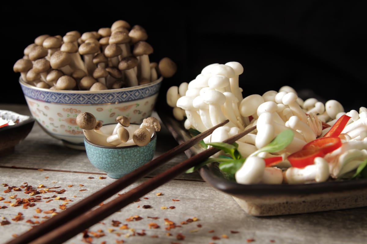 White and brown beech mushrooms in various bowls atop a wooden backdrop.