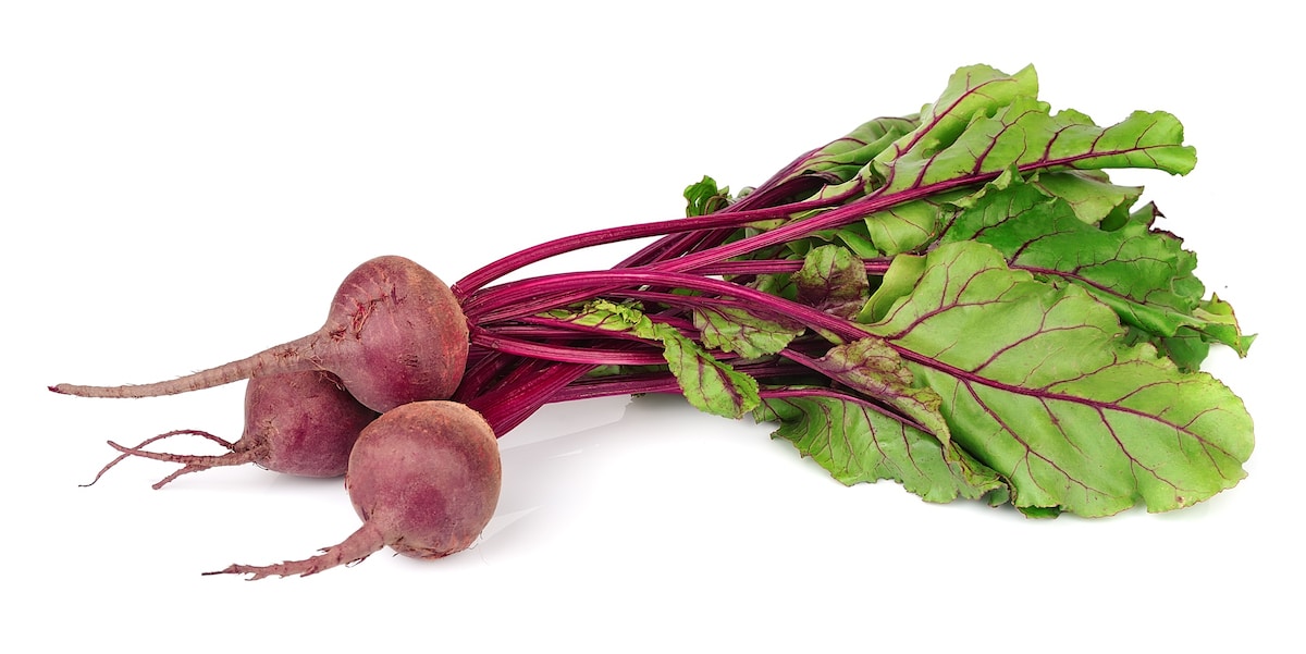 Three whole beets with beet greens attached on a white background.