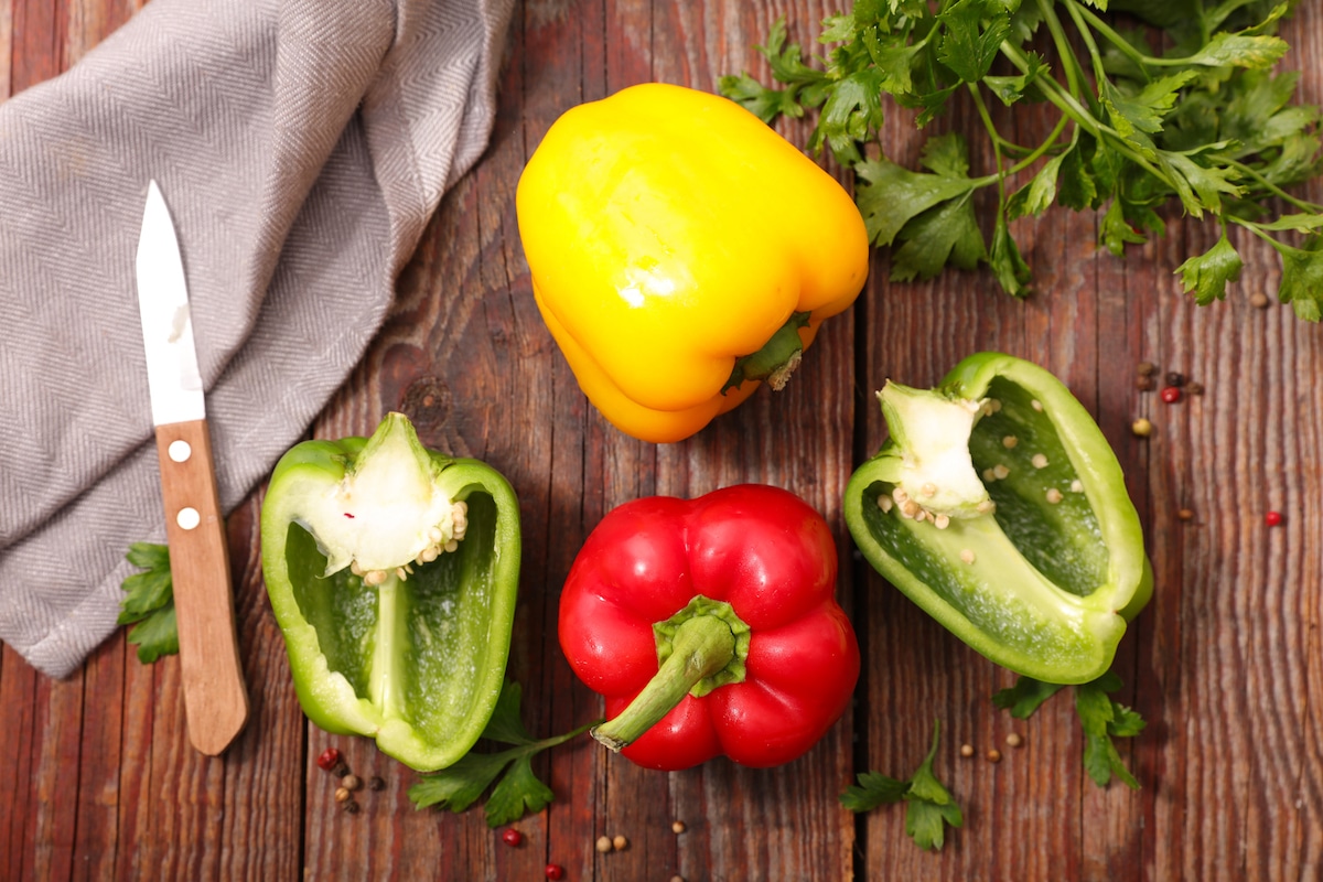 Raw whole red, yellow, and green bell peppers on a wooden background