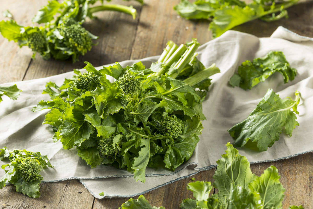 Several bunches of raw broccoli rabe on a tan towel on top of a wooden background