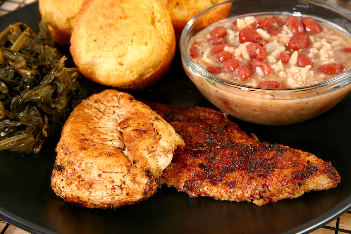 Blackened catfish and chicken with cajun side dishes on a black plate