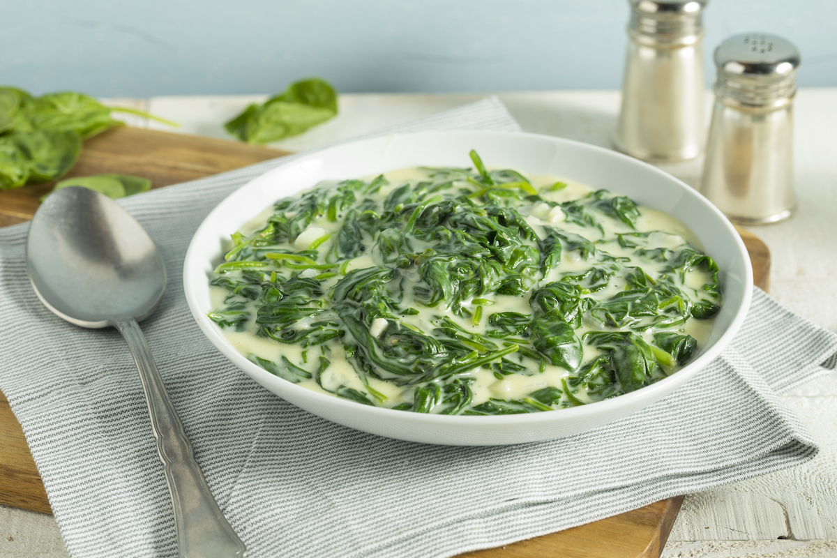 Creamed spinach in a white bowl with a striped napkin underneath