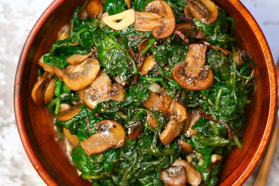 sauteed power greens and mushrooms in a small wooden bowl