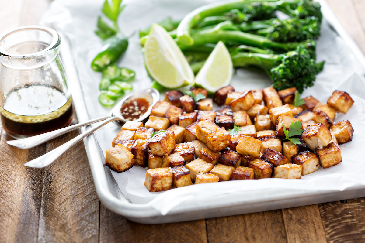 pan fried tofu cubes on a baking sheet with broccolini and limes