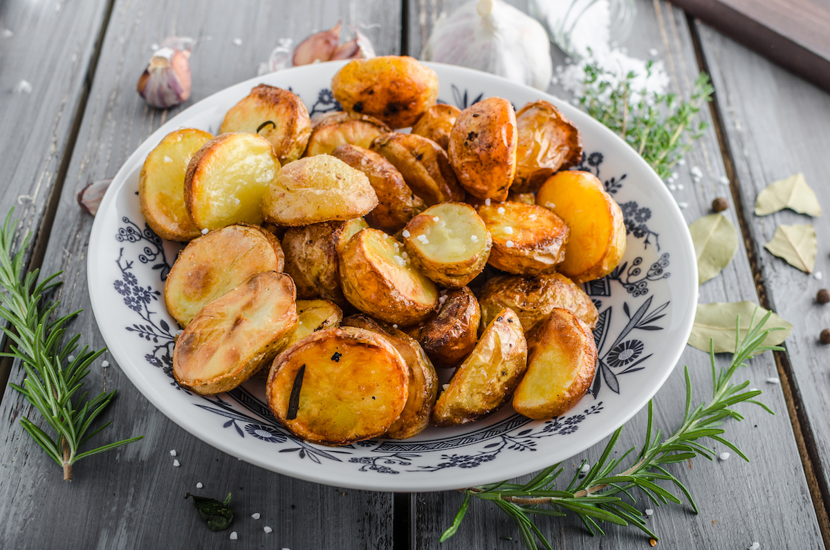 oven roasted potatoes in a white bowl surrounded by rosemary sprigs